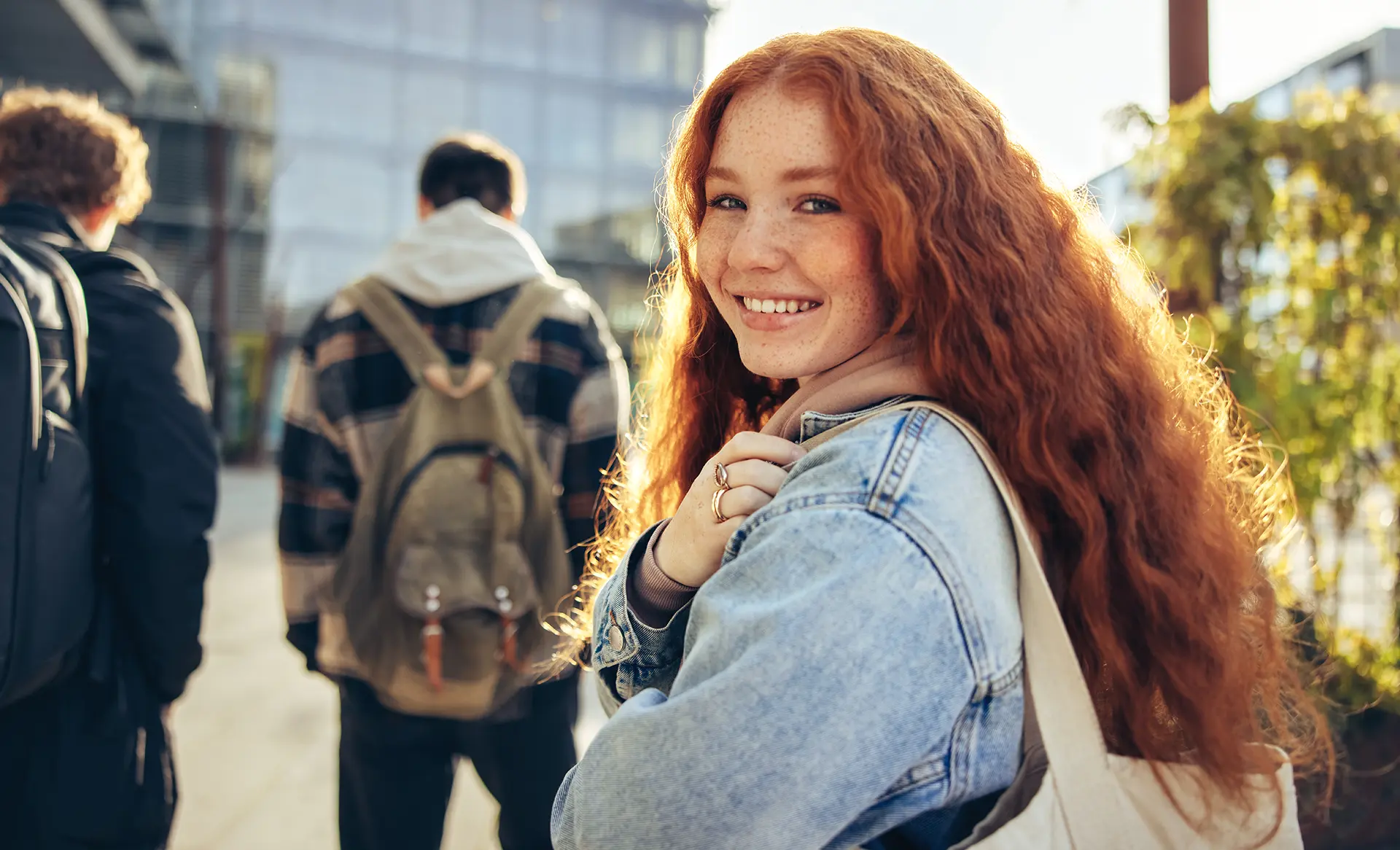 several students walking to class outside building, one student facing camera is smiling