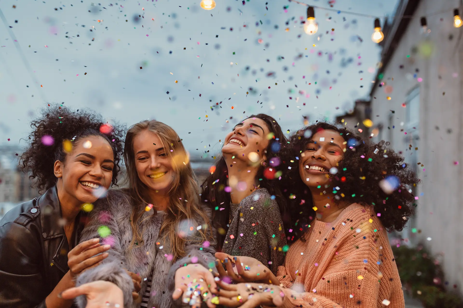 four happy friends throwing multi-colored confetti in the air